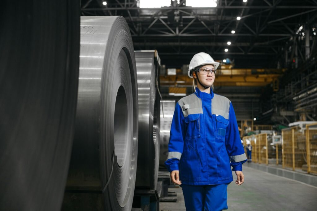 Female industrial worker in protective gear at a steel manufacturing facility.